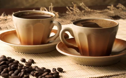 HD PC desktop wallpaper showing two cups of coffee on saucers with coffee beans scattered nearby, highlighting a warm and inviting food and coffee theme.