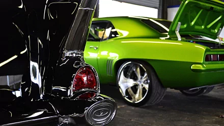 A striking green Chevrolet Camaro showcases its sleek design alongside a classic black vehicle, set in a garage, designed as an HD desktop wallpaper.
