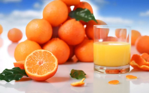 HD desktop wallpaper featuring a vibrant arrangement of fresh oranges with a glass of orange juice against a soft blue sky background.
