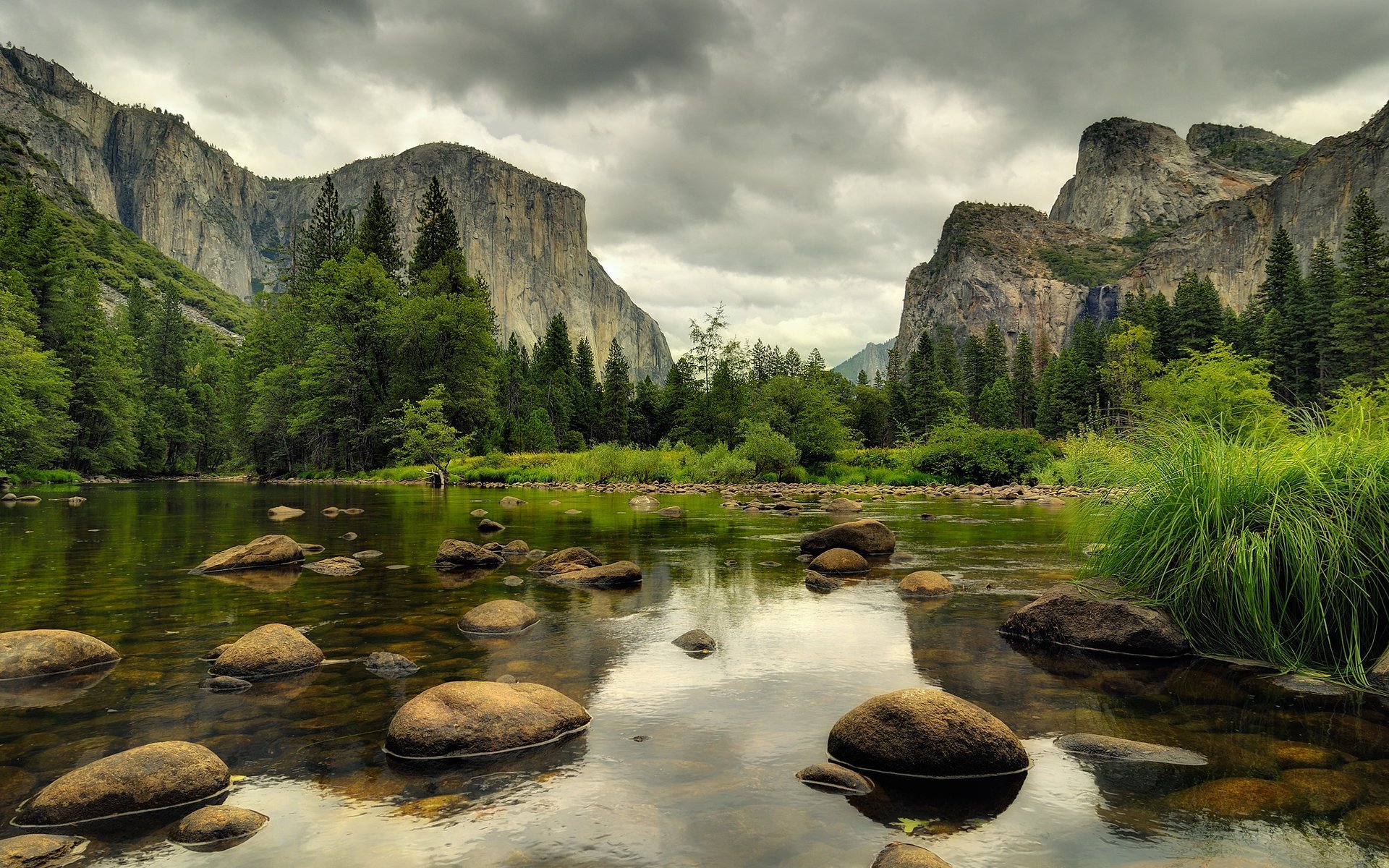 A serene landscape featuring a tranquil river surrounded by towering mountains and lush trees, captured in rich detail—an HD desktop wallpaper celebrating the beauty of nature.