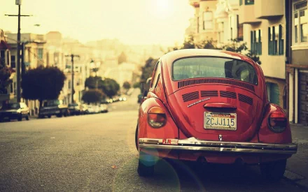 A vibrant red Volkswagen Beetle parked on a quiet street, bathed in warm sunlight, creating a nostalgic and inviting atmosphere in this HD desktop wallpaper.