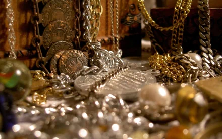 A close-up view of an array of jewelry, coins, and ornaments in gold and silver, showcasing intricate designs and textures, set against a richly detailed background. HD desktop wallpaper.