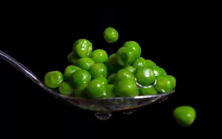 Close-up HD desktop wallpaper of fresh green peas on a spoon against a black background.
