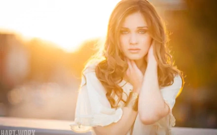 HD desktop wallpaper featuring a beautiful woman with long wavy hair, bathed in warm golden sunlight, against a blurred background.