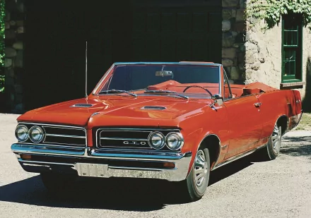 HD desktop wallpaper featuring a classic red Pontiac GTO convertible parked in front of a stone building.