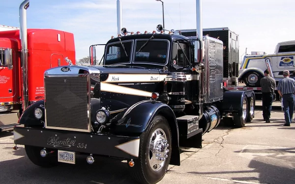 HD desktop wallpaper featuring a classic black Mack truck parked outdoors among other vehicles at a truck show.