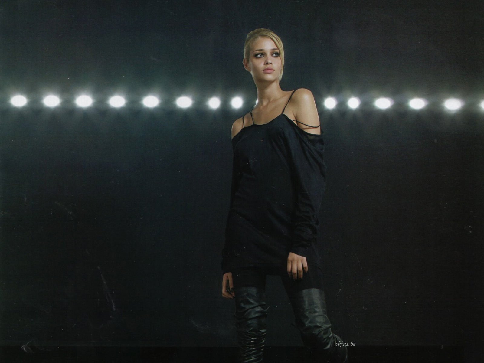 HD PC desktop wallpaper showing a woman in an off-shoulder black dress standing beneath a row of bright stage lights against a dark, textured background.