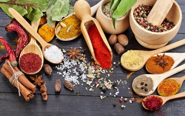 A vibrant assortment of herbs and spices arranged on a dark wooden surface, featuring various bowls and spoons filled with colorful ingredients, creating a rich culinary backdrop.