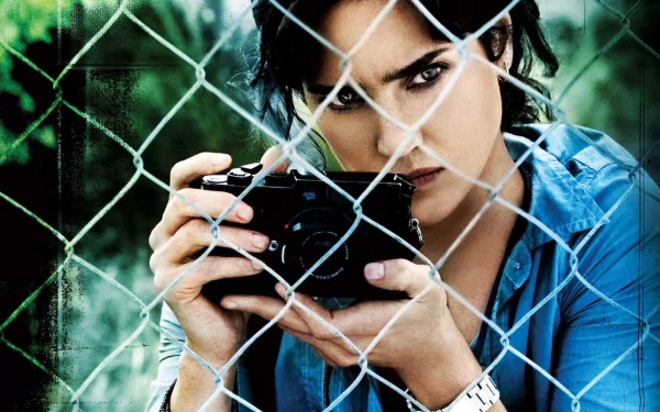 HD desktop wallpaper featuring Jennifer Connelly from Blood Diamond, intensely focusing through a camera, behind a chain-link fence.