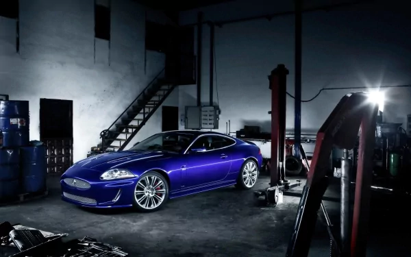 A sleek blue Jaguar car parked inside a dimly lit garage, captured in a high-definition PC desktop wallpaper showcasing the vehicle's design and surroundings.