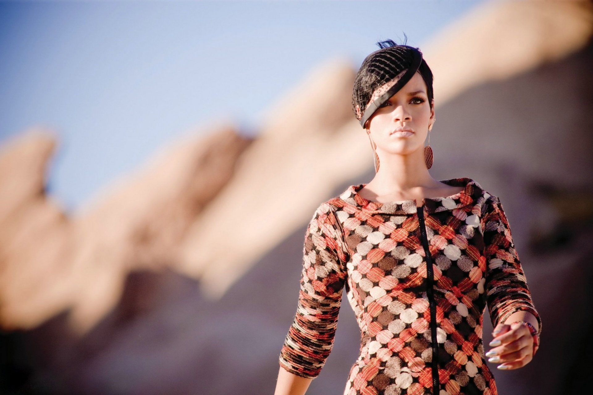 HD PC desktop wallpaper featuring Rihanna in a patterned outfit against a blurred natural rock background, capturing a music-inspired stylish portrait.