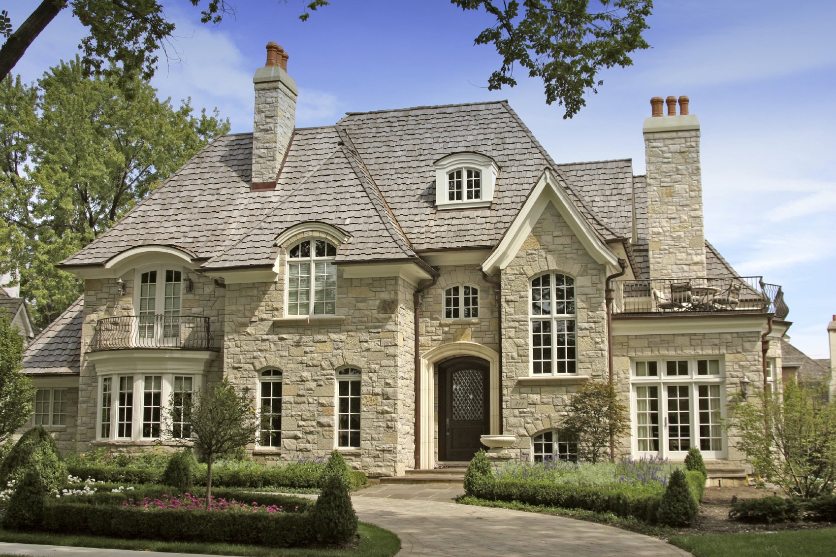 HD PC desktop wallpaper of a large, elegant man-made stone house with multiple chimneys, arched windows, and a manicured garden under a clear blue sky.
