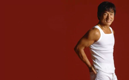 HD wallpaper featuring celebrity Jackie Chan against a red background, wearing a white sleeveless shirt and pants, smiling confidently.