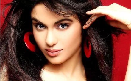 A high-definition wallpaper featuring Adah Sharma with flowing dark hair and striking red earrings, set against a vibrant red background.