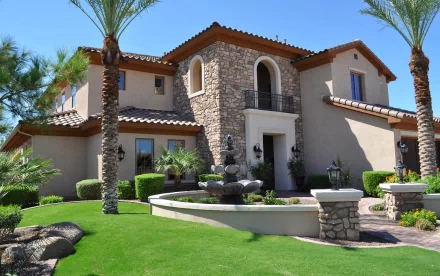 A stunning man-made house features elegant stonework and lush landscaping, complemented by palm trees and a tranquil fountain, captured in vibrant 4K Ultra HD.