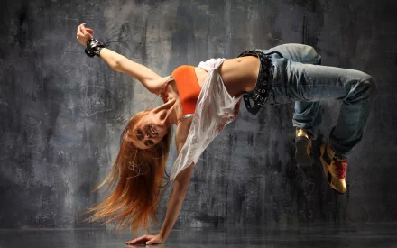 A dancer in mid-air performs a dynamic move against a textured gray background, set as an HD desktop wallpaper. The movement and energy of the dancer epitomize the rhythm of music and dance.