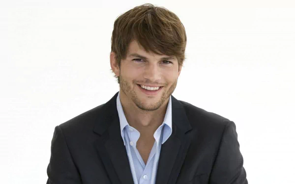 2K Quad HD PC desktop wallpaper: portrait of a smiling young man with short brown hair wearing a dark blazer and open-collar light shirt against a white background.