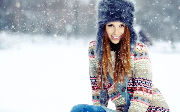 Beautiful woman in a colorful sweater and fur hat smiles amidst falling snow, captured in stunning 4K Ultra HD for a vivid PC desktop wallpaper.