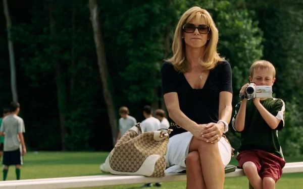 HD desktop wallpaper featuring Sandra Bullock from the movie The Blind Side, sitting outdoors with a young boy filming beside her.