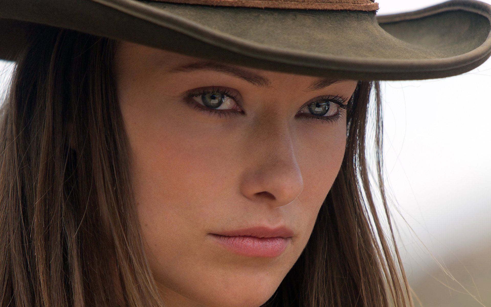 HD PC desktop wallpaper featuring a close-up portrait of celebrity Olivia Wilde wearing a hat, showcasing her intense gaze and natural makeup.