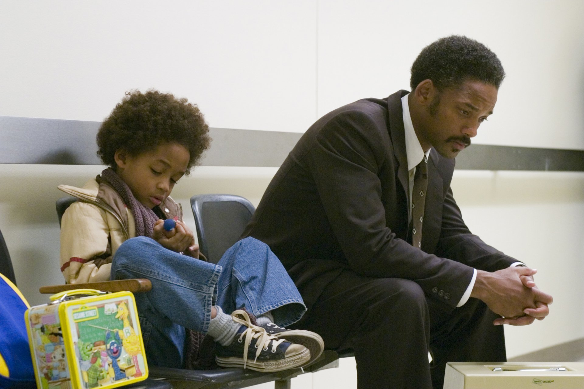 A poignant scene from The Pursuit of Happyness, featuring Jaden Smith and Will Smith. They sit together, reflecting their characters' struggles and bond in a moment of quiet intensity.