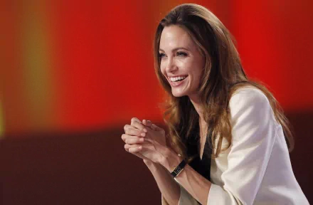 A vibrant 4K Ultra HD desktop wallpaper featuring celebrity Angelina Jolie, smiling and engaged, radiating warmth against a striking red background.