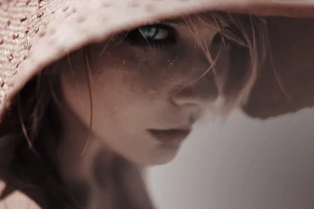 A high-definition wallpaper showing a close-up of a woman's face partially shaded by a wide-brimmed hat, creating a dramatic and mysterious effect.