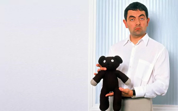 HD PC desktop wallpaper featuring celebrity Rowan Atkinson holding a black teddy bear with a neutral expression against a simple background.