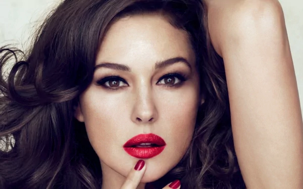 A stunning HD desktop wallpaper featuring Monica Bellucci with glamorous makeup and tousled hair, highlighting her captivating gaze and bold red lips.