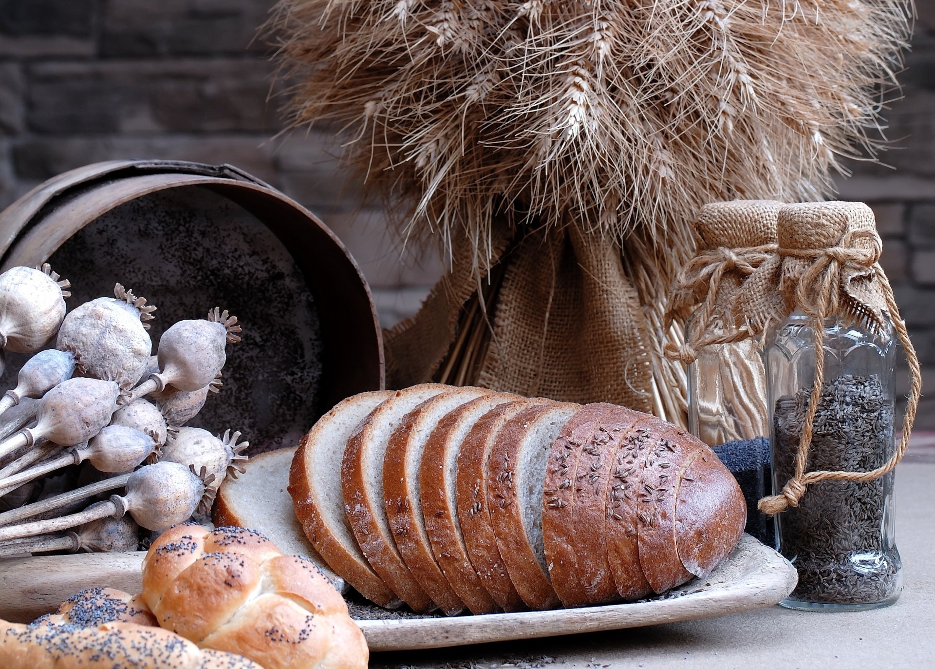 HD desktop wallpaper featuring rustic bread slices on a plate, accompanied by dried wheat stalks, a jar of seeds, and a bowl of garlic bulbs, set against a dark background.