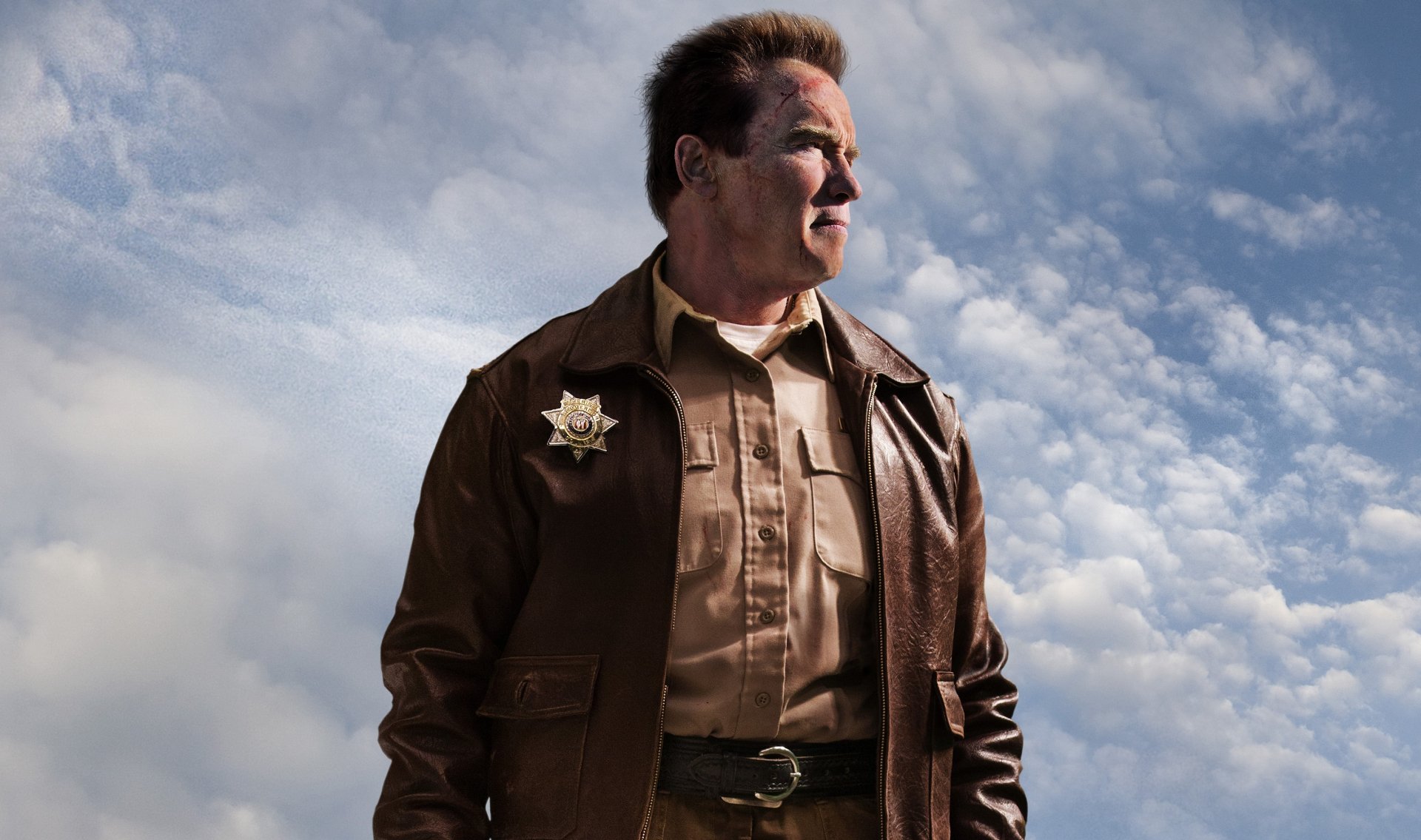 HD PC desktop wallpaper featuring celebrity Arnold Schwarzenegger in a sheriff uniform against a cloudy sky background.