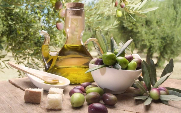A clear, high-definition image of a jar of olive oil beside a bowl of fresh olives and bread, set against a backdrop of olive trees, showcasing the beauty of food and nature.