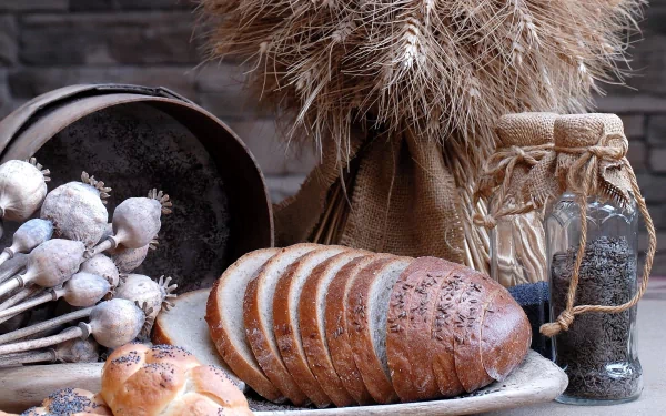 HD desktop wallpaper featuring rustic bread slices on a plate, accompanied by dried wheat stalks, a jar of seeds, and a bowl of garlic bulbs, set against a dark background.