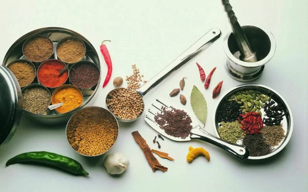 HD desktop wallpaper featuring a vibrant array of herbs and spices arranged with measuring spoons and a mortar and pestle on a white background.