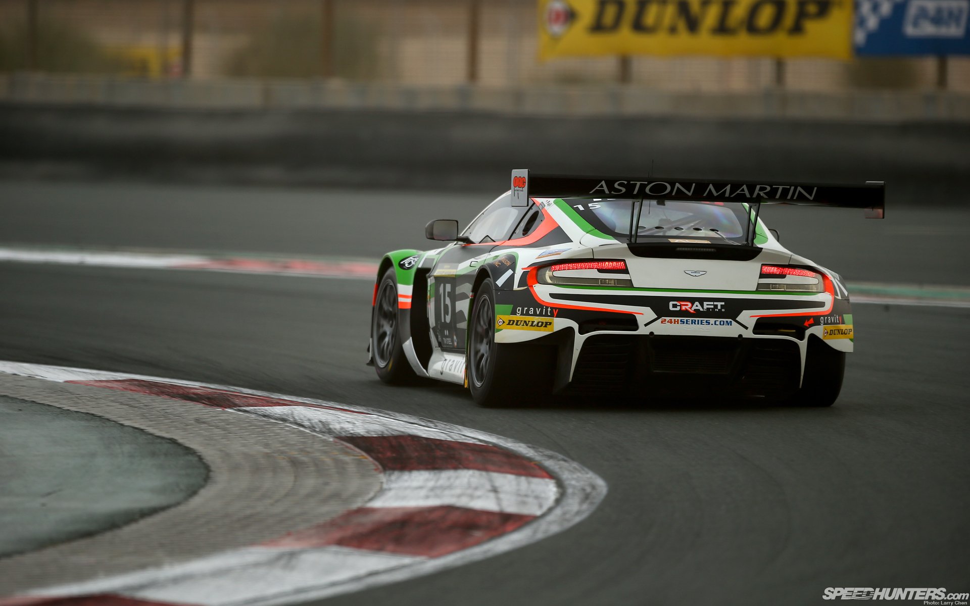 HD PC desktop wallpaper/background: rear view of an Aston Martin GT race car hugging a curving racetrack, Dunlop signage blurred in the background.