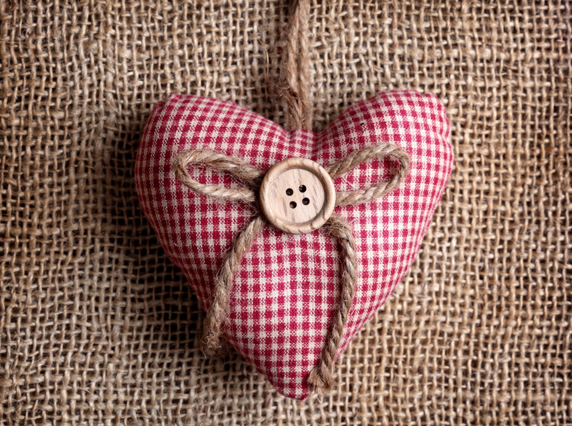 Artistic 4K Ultra HD wallpaper featuring a red gingham fabric heart ornament with a button and twine bow on a textured burlap background.