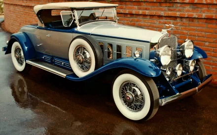 A classic blue and beige Packard vehicle with whitewall tires, showcased as a Cadillac V16, set against a brick wall background in this HD PC desktop wallpaper.