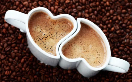 Two heart-shaped coffee cups filled with rich coffee, surrounded by roasted coffee beans, create a warm and inviting desktop wallpaper for coffee lovers.