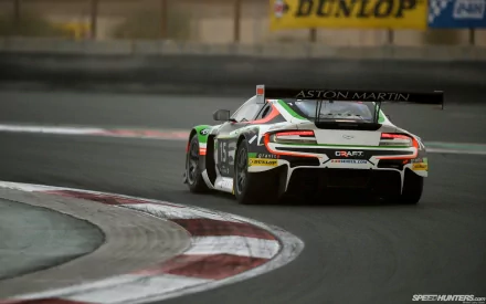 HD PC desktop wallpaper/background: rear view of an Aston Martin GT race car hugging a curving racetrack, Dunlop signage blurred in the background.