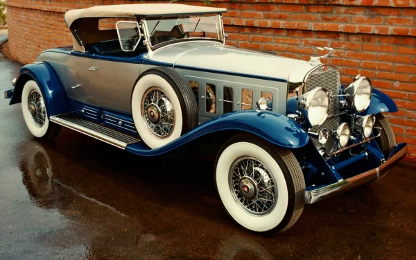 A classic blue and beige Packard vehicle with whitewall tires, showcased as a Cadillac V16, set against a brick wall background in this HD PC desktop wallpaper.