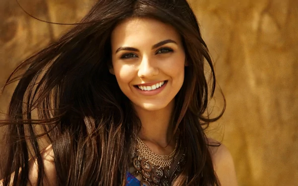 HD desktop wallpaper featuring actress Victoria Justice with brunette hair and brown eyes, smiling against a warm, earthy background.