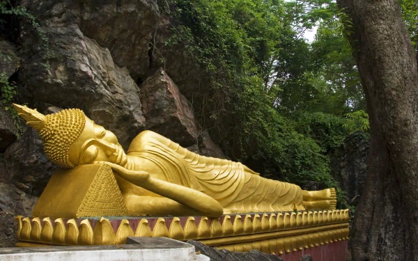 A serene image of a golden reclining Buddha statue nestled against a rocky backdrop, surrounded by lush greenery, capturing the essence of Buddhism in a tranquil setting.