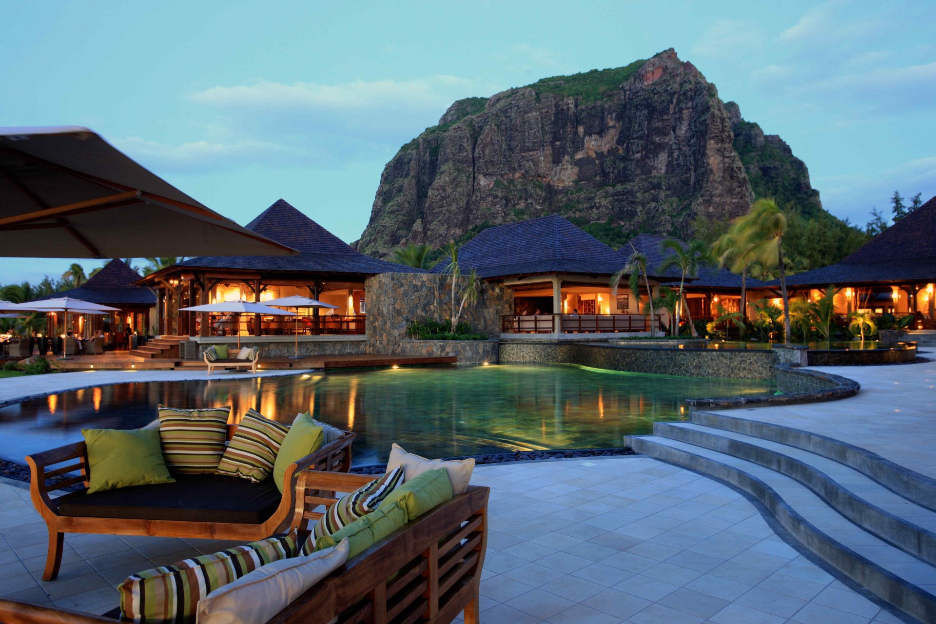 4K Ultra HD image of a man-made resort featuring a luxurious pool area, cozy outdoor seating, and a large mountain backdrop under a clear sky.