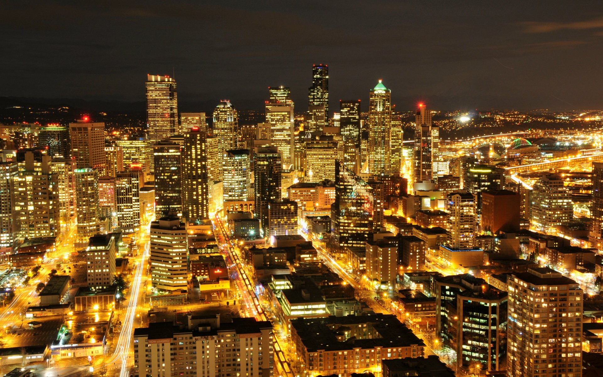 Night aerial view of Seattle skyline with illuminated skyscrapers and streets, HD PC desktop wallpaper background showcasing a man-made urban landscape.