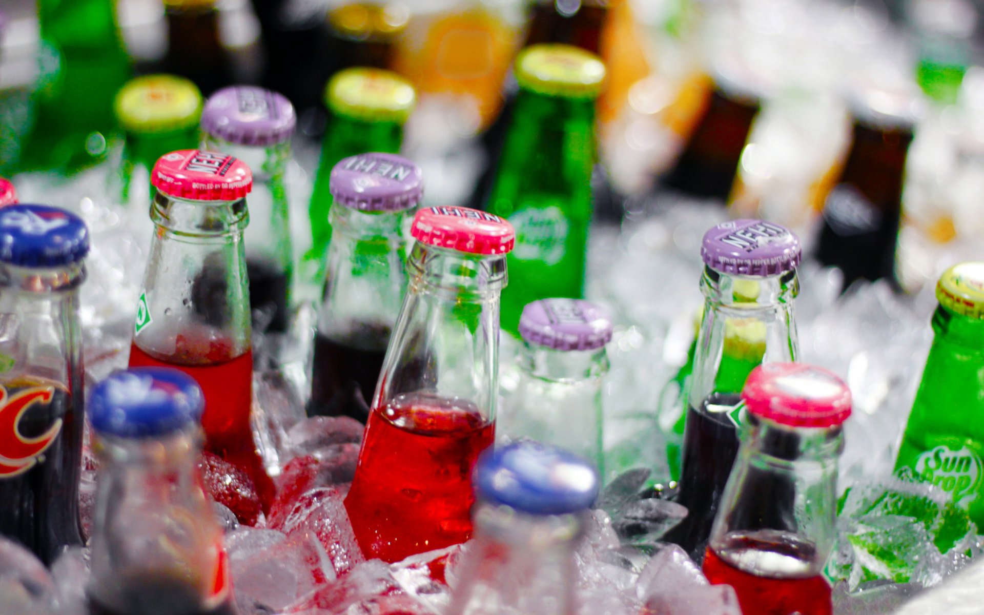 2K Quad HD PC desktop wallpaper and background: colorful glass soda bottles and caps chilled in crushed ice, a vivid food and drink scene.