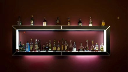 A sleek display shelf featuring a variety of liquor bottles against a deep-colored wall, creating an atmospheric setting for food and drink enthusiasts. HD desktop wallpaper background.