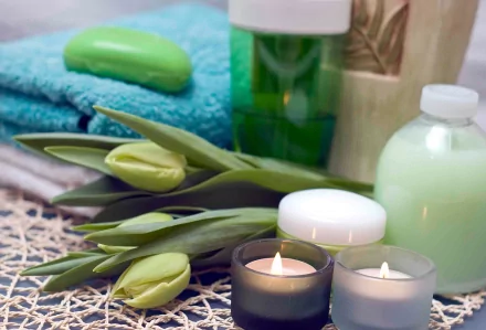 Man-made spa scene with lit candles, lotion bottles, fresh tulips and folded towels — 2K Quad HD PC desktop wallpaper and background.