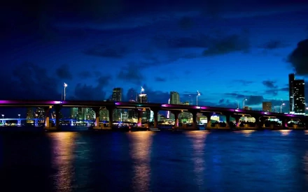 Night view of a man-made bridge in Miami, Florida, with city lights reflecting on the water under a deep blue sky, captured in HD for a desktop wallpaper.