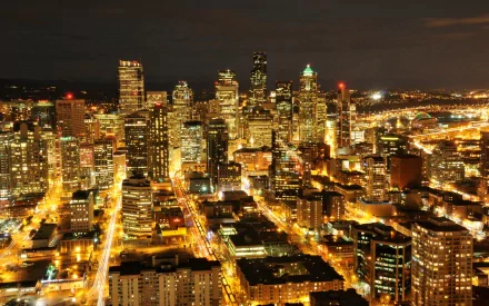 Night aerial view of Seattle skyline with illuminated skyscrapers and streets, HD PC desktop wallpaper background showcasing a man-made urban landscape.