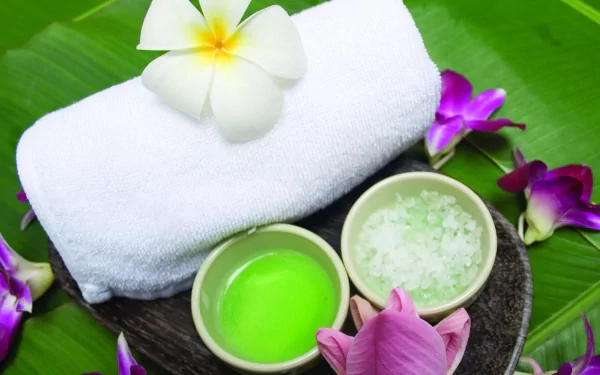 2K Quad HD PC desktop wallpaper of a man-made spa arrangement: white towel, bowls of green oil and bath salts, frangipani and orchid flowers on a banana leaf.